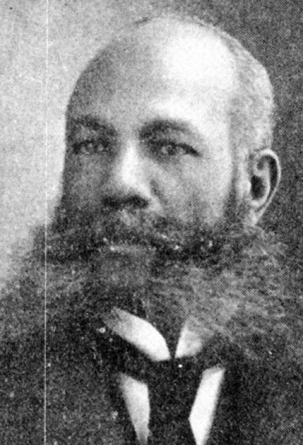Man with long mustache and beard, bald, and wearing a suit and tie